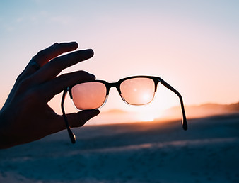 Stock photo of left hand holding a pair of sunglasses during sunrise.