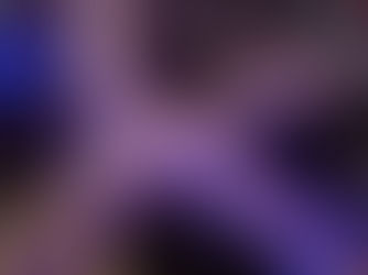 Night aerial view of a sprawling freeway interchange in a city, glowing with purple and blue lights, city buildings in the background.