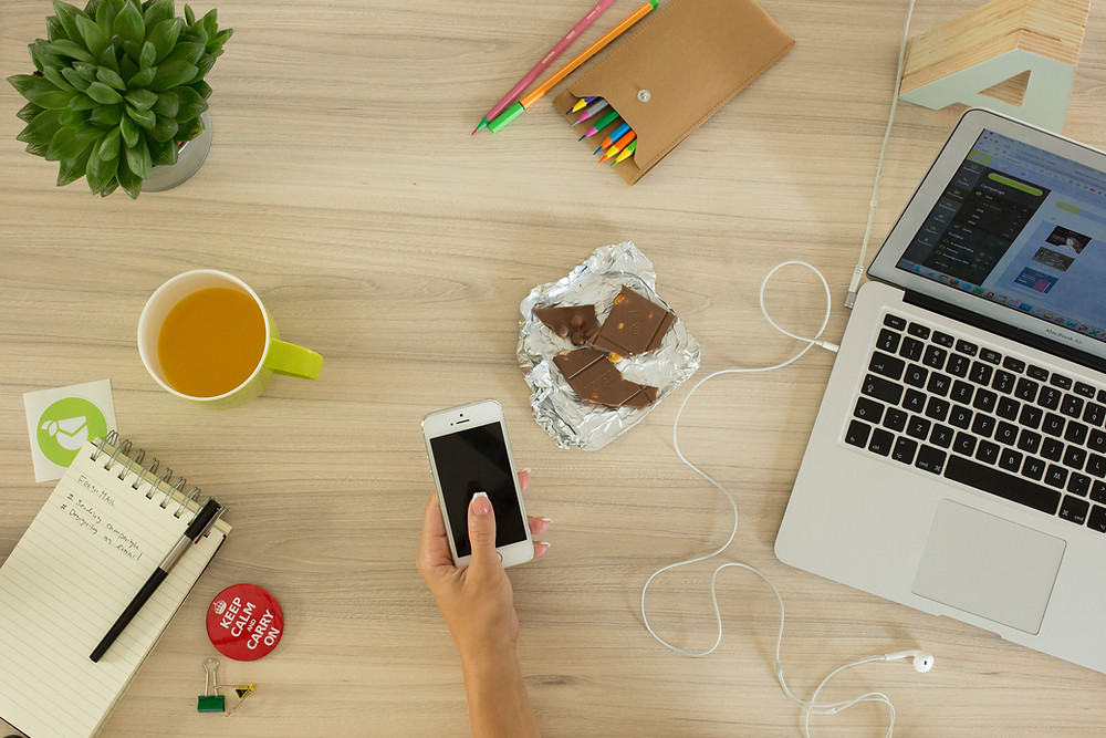 Person holding phone and using computer to get work done at desk