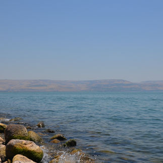 Gentle waves hitting the basalt rocks of the Sea of Galilee with the Golan Heights in the distance.