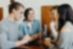 Four young professionals smiling and collaborating at a table with laptops and coffee.
