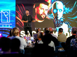 Speaker on stage with futuristic AI graphics, addressing an audience. Blue and red visuals with CHATA logo, text reads "THE FUTURE."