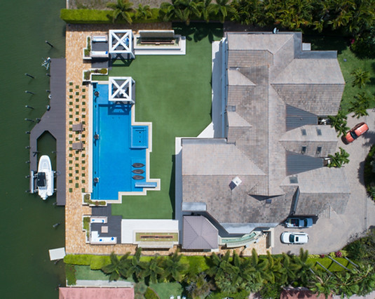 Aerial view of a mansion featuring a pool, yacht, and garden, captured by Derek Thomson.