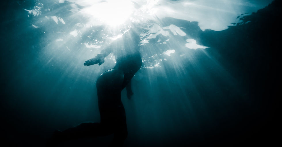 Image of a person in water pushing themselves up to the surface toward the light.
