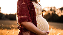 A pregnant woman standing in a golden field with her hands on her baby.