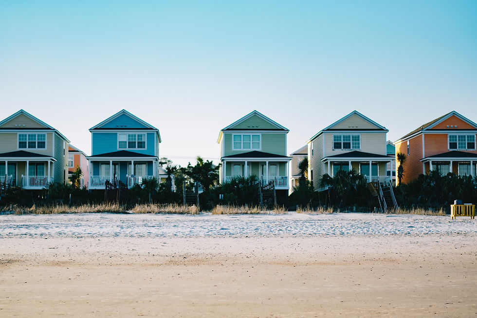 Colorful beach houses lined up along a sandy shore, with a clear blue sky in the background. Coastal and serene setting.