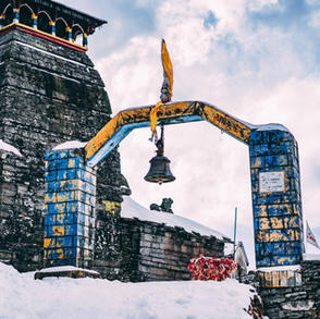 A view of the Tungnath temple located at a high altitude surrounded by snow-capped Himalayan peaks and green valleys.