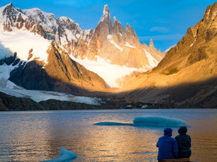 two exporers looking at across a lake at a snow capped mountain