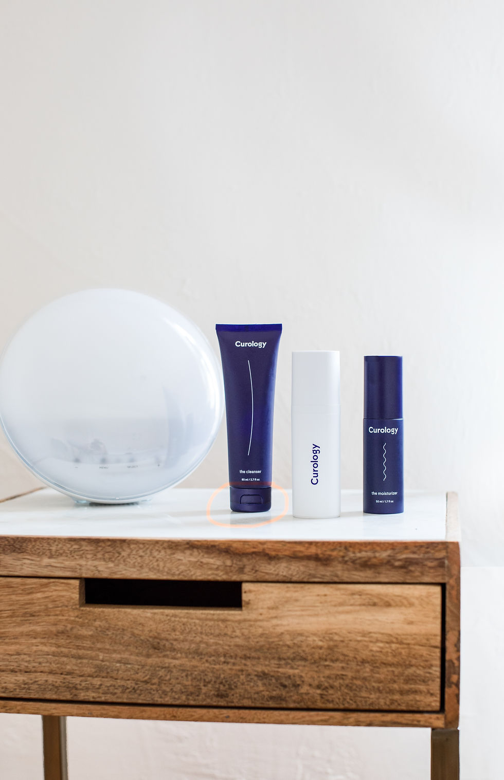 Curology skincare bottles on a wooden table beside a frosted globe lamp, with cleanser and moisturizer text on a bright white background