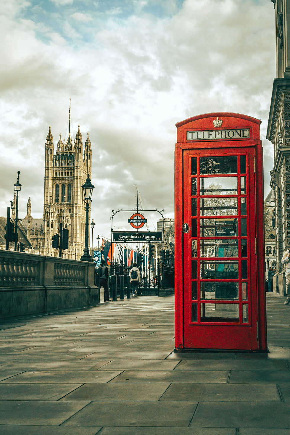 Cabine téléphonique rouge à Westminster, près du métro, avec Big Ben et le Parlement sous un ciel nuageux.