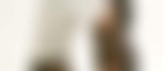 Man in white pants wearing brown loafers with gold detailing, standing on a light, neutral background. Shoes have thick black soles.