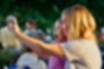 Woman and child taking a selfie outdoors, both smiling brightly. The child is wearing a pink top. Blurred people and greenery in the background.