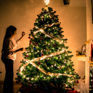 A woman placing an ornament on a decorated Christmas tree