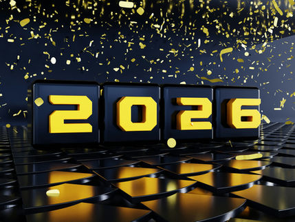 Black blocks with yellow "2026" text on a reflective surface, surrounded by falling gold confetti against a dark background. Festive mood.