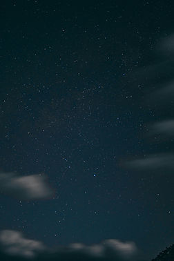 Night sky filled with stars, scattered clouds moving across, dark horizon at bottom. Calm, serene atmosphere.