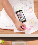Man sits at desk making plans on paper with mobile phone in view. Image by Firmbee.com