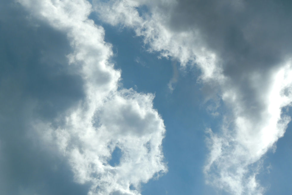 Looking up at patchy white and shaded grey clouds breaking to reveal patches of blue sky on an autumn day.