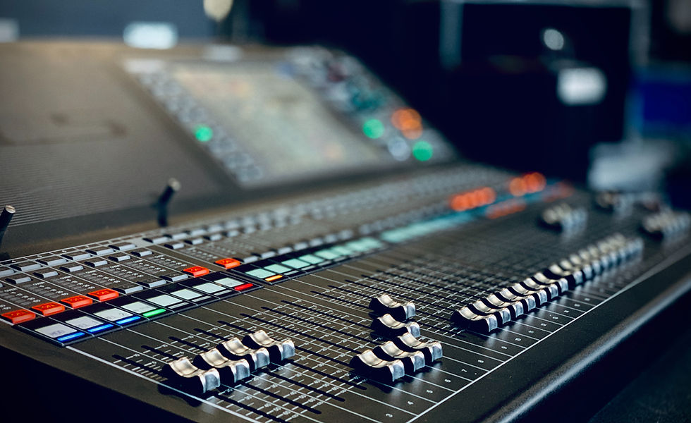 Close-up of a sound mixing console with colorful buttons and sliders in a dimly lit studio.
