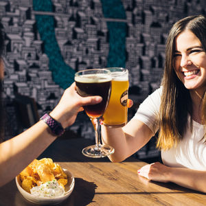 Two women sitting at a table toasting with glasses of beer