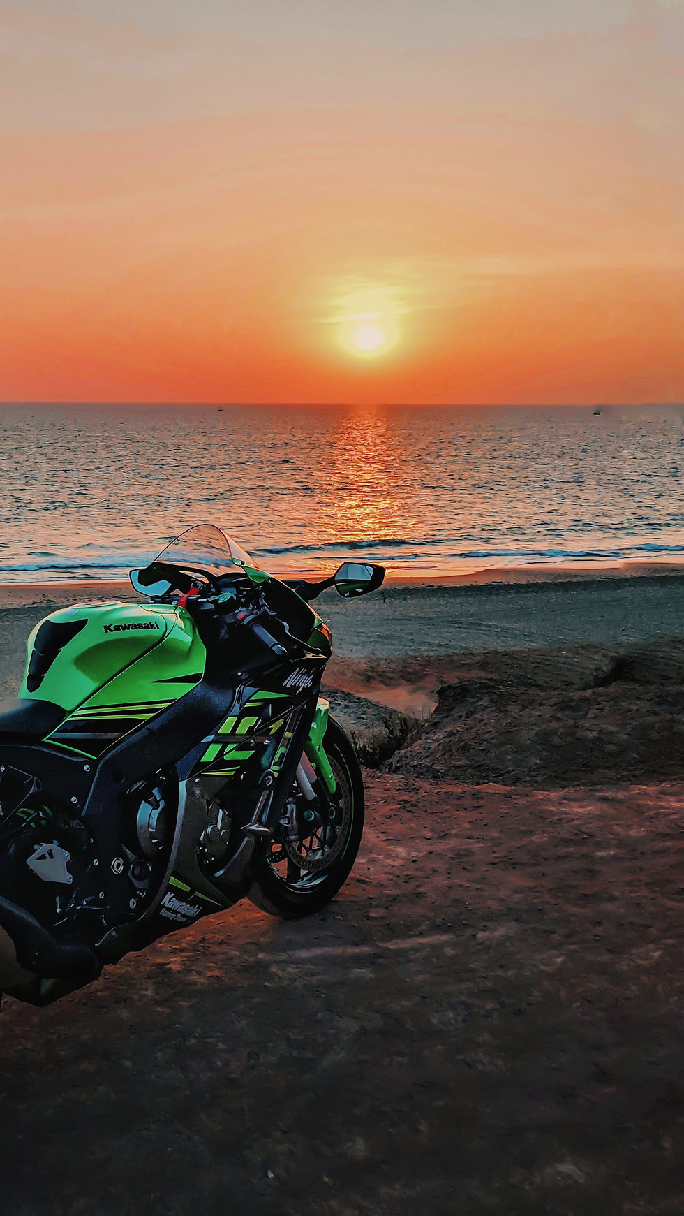 Green motorcycle parked on the beach at sunset