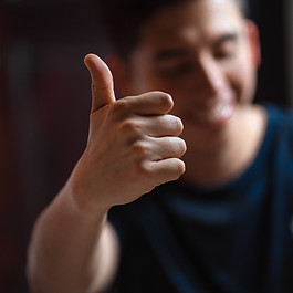 A smiling person holds up a fist displaying a thumbs up sign