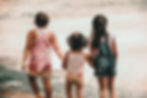 Three little girls holding hands exploring waves. Picture is from behind them as they approach the waves.