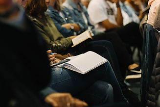 zoomed in image of open notebooks on laps of poeple sitting in chairs