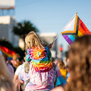 A child waving a trans flag being carried through a Pride Parade