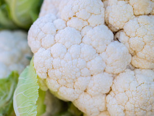 Close-up of a cauliflower with green leaves. The cauliflower's surface is bumpy and off-white, contrasting with the vibrant green leaves.