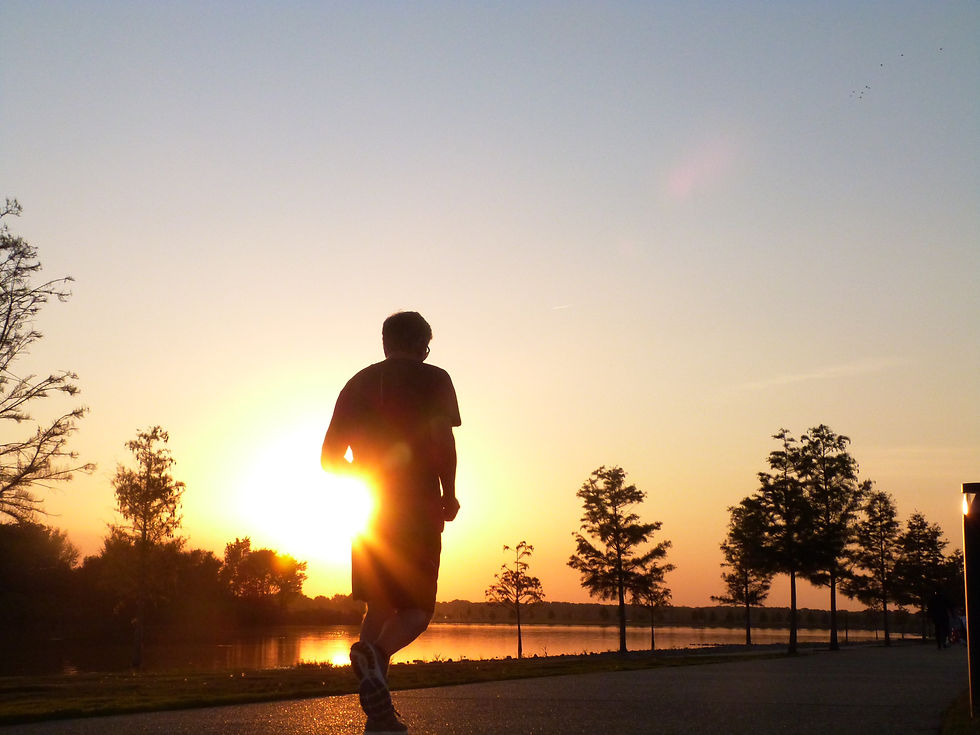 Silhouetted person walking at sunset beside a lake, with trees and glowing orange sky reflected on the water.