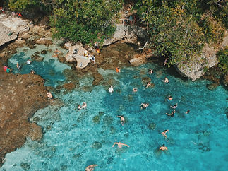 Aerial view of people swimming in clear turquoise water surrounded by coral reefs