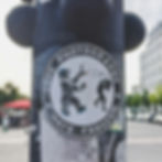 Sticker on a pole shows a bear with a camera facing a person, with "LOVE PHOTOGRAPHY HATE FASCISM" text. Urban street in the background.
