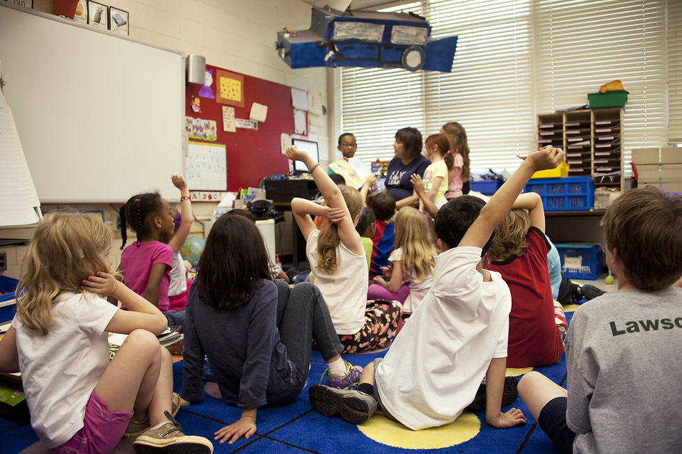 Classroom of students sitting on a carpet raising their hands