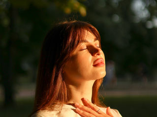 A woman taking a deep breath with eyes closed, looking up at sunset.