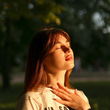 A woman taking a deep breath with eyes closed, looking up at sunset.