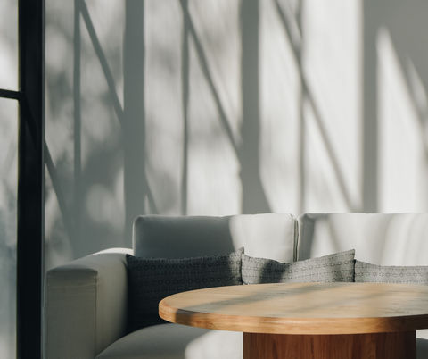 Cozy minimalist living room with tall window and sun casting shadows on wall