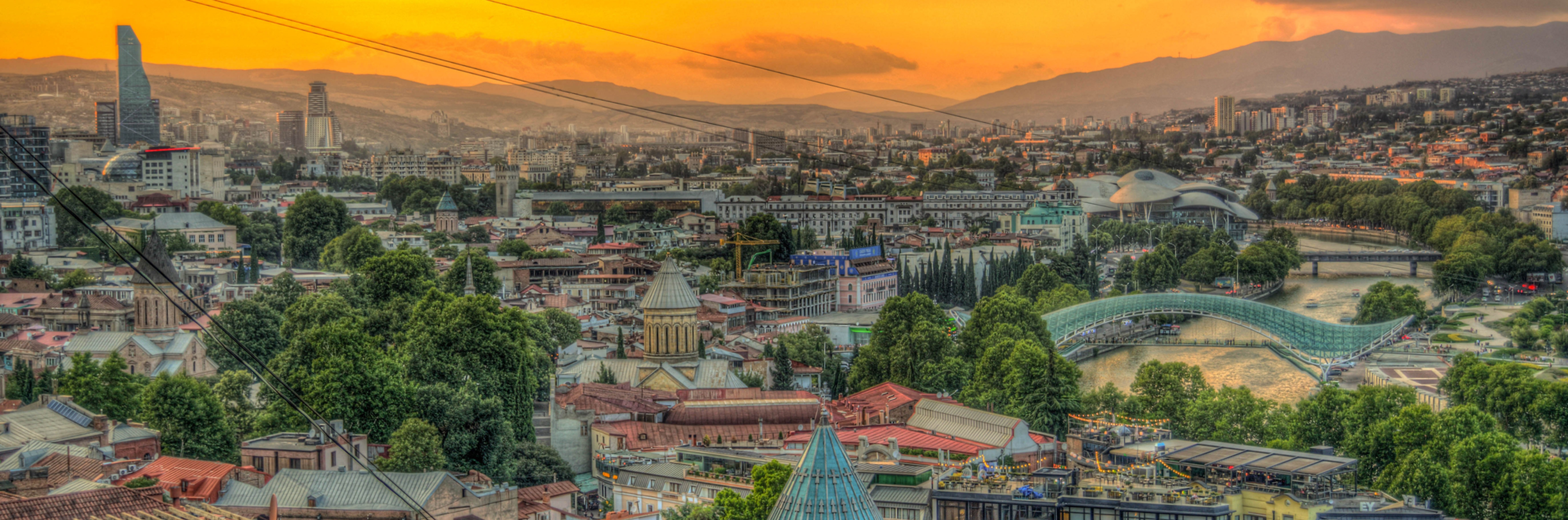 Sunset over Tbilisi in summer with the iconic Bridge of Peace arching over the Mtkvari River.