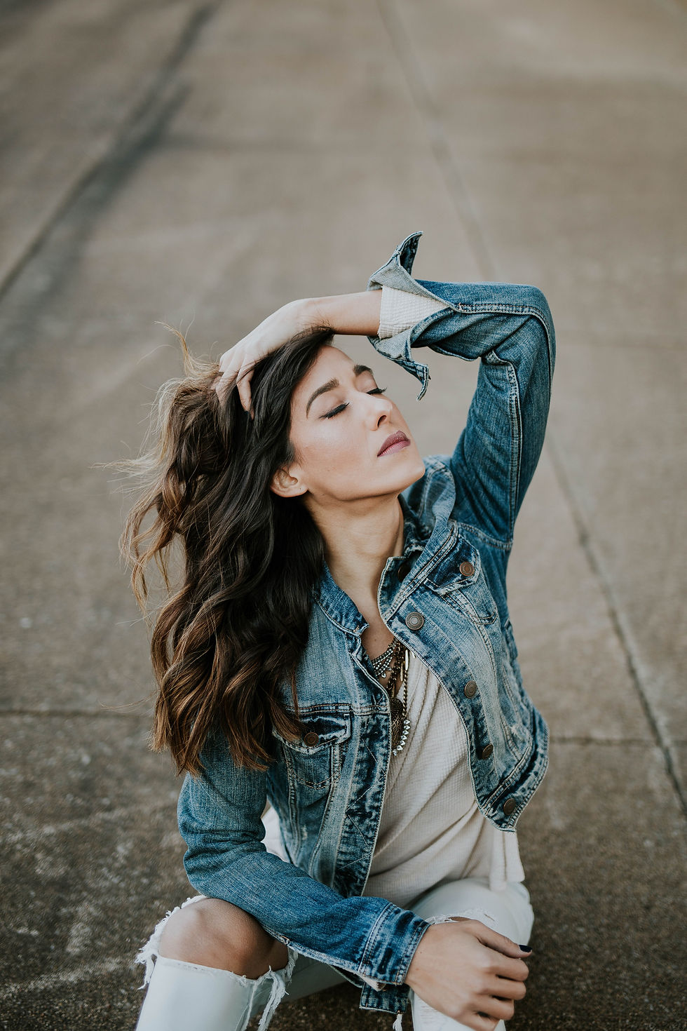 woman sitting on a conrete floor, her left hand is in her hair