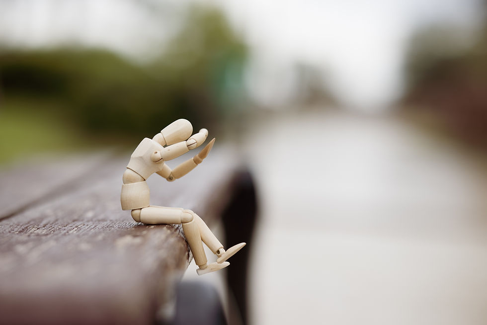 A picture of a wooden figure sitting on a bench, hes looking frightened.