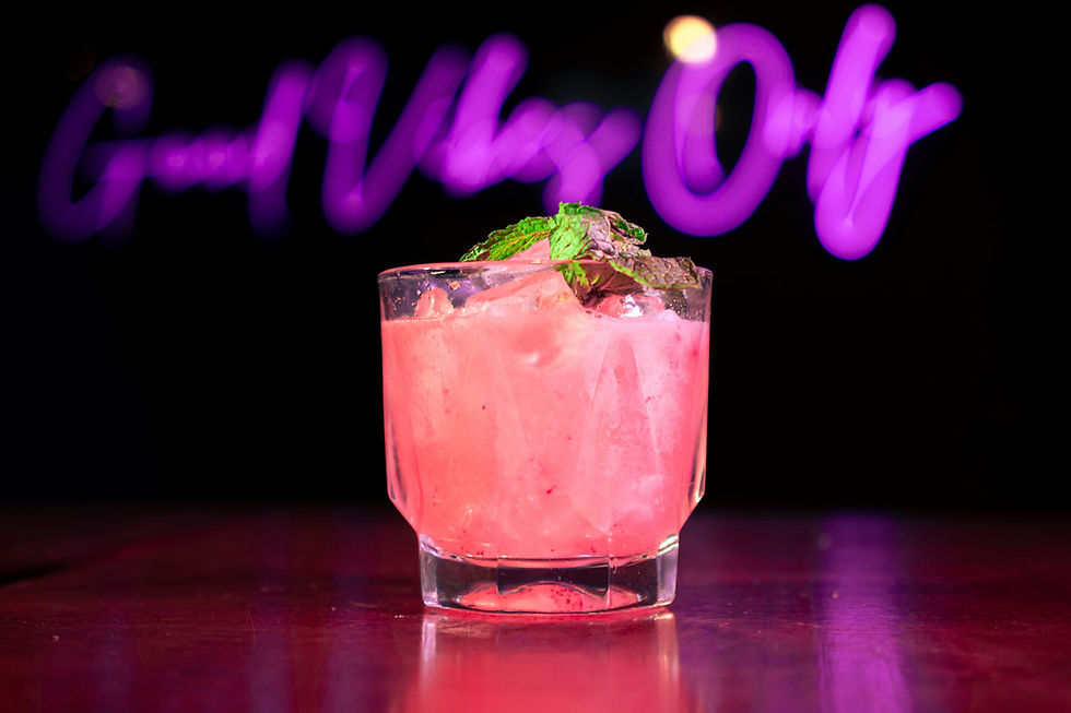 A pink cocktail with a neon sign behind saying good vibes only
