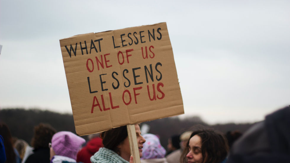 A photo of a protest sign saying "What lessens one of us lessens all of us", representing resistance towards Migration detention in Europe.