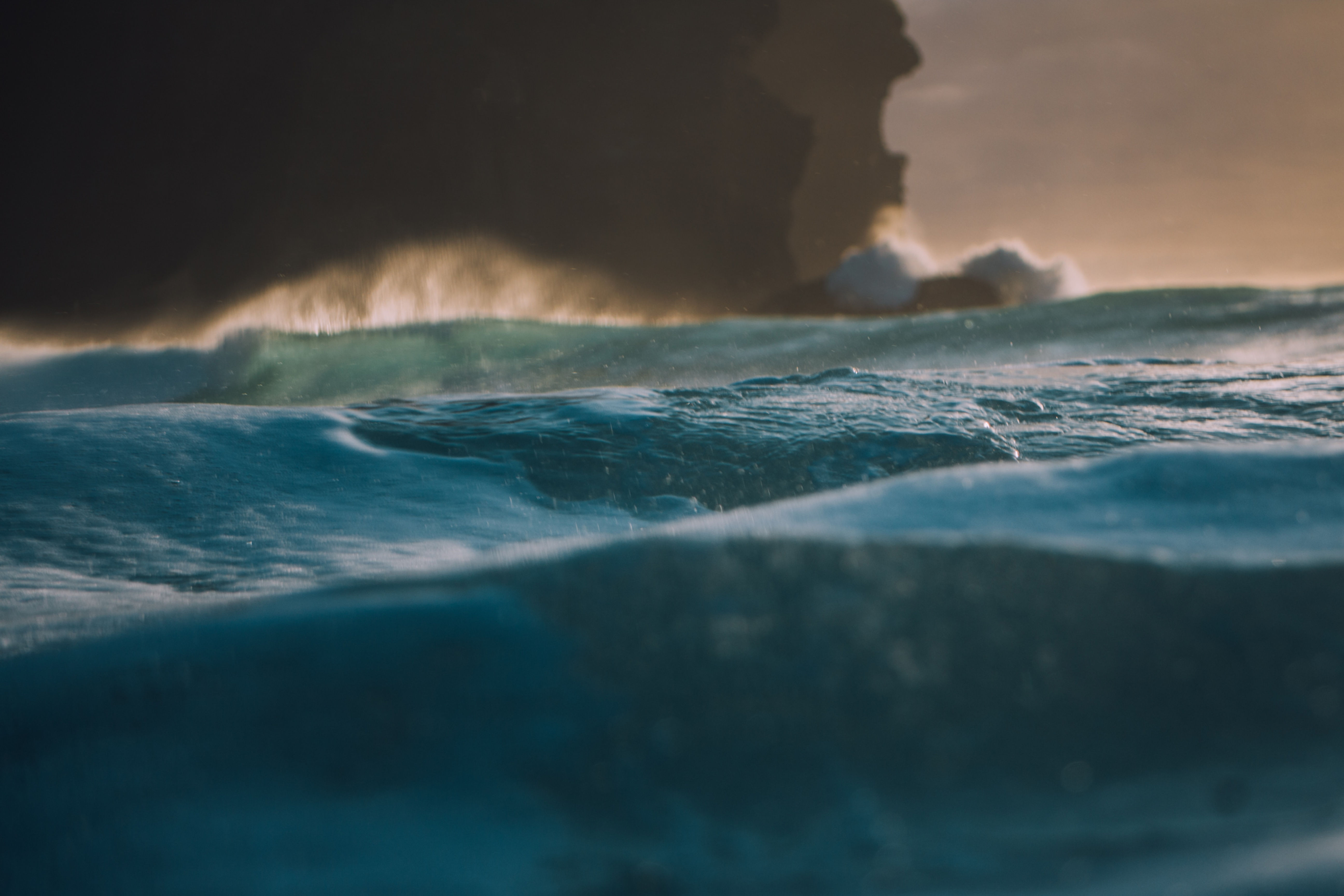 close up of deep blue, green ocean with view of brown sandy moutain in the background