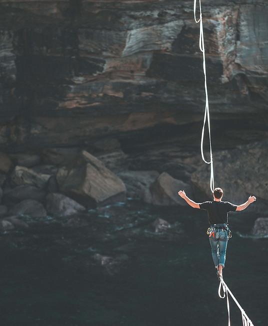 Symbolisches Bild für Risikomanagement – Mann auf Slackline mit Sicherungsseil in Felslandschaft