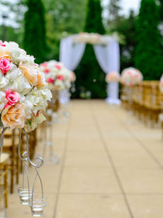 An aisle of chairs at a wedding ceremony decorated with flowers leading to a curtain and floral backdrop.