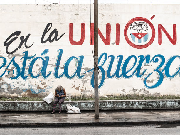 Un murale cubano con la scritta 'En la UNIÓN está la fuerza' e una persona che cammina accanto.