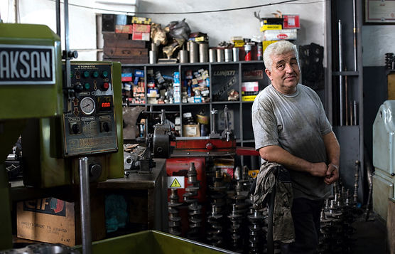 A business owner stands pensively in a busy workshop, surrounded by machinery and tools, considering the prospect of selling the business.