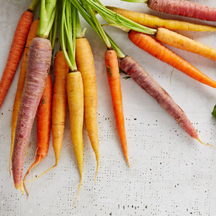 A bunch of multicolored carrots, including orange, yellow, and purple, on a speckled gray surface. A green leaf lies nearby.