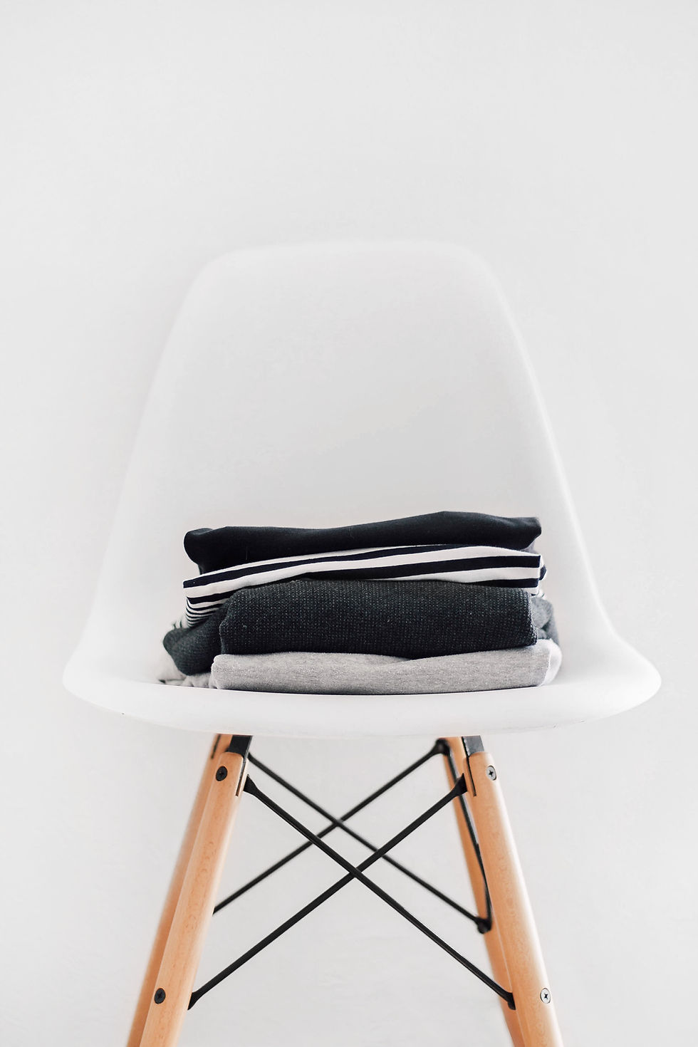 A white chair with a small pile of black and grey clothes neatly folded on top.