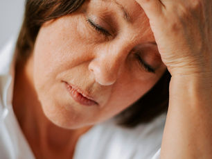 A woman looks fatigued and stressed, resting her hand on her forehead with her eyes closed, reflecting a moment of exhaustion.