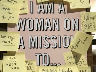 The image shows a poster with the title "Woman on a mission to", it is surrounded by yellow post it note's displaying targets & goals written down .